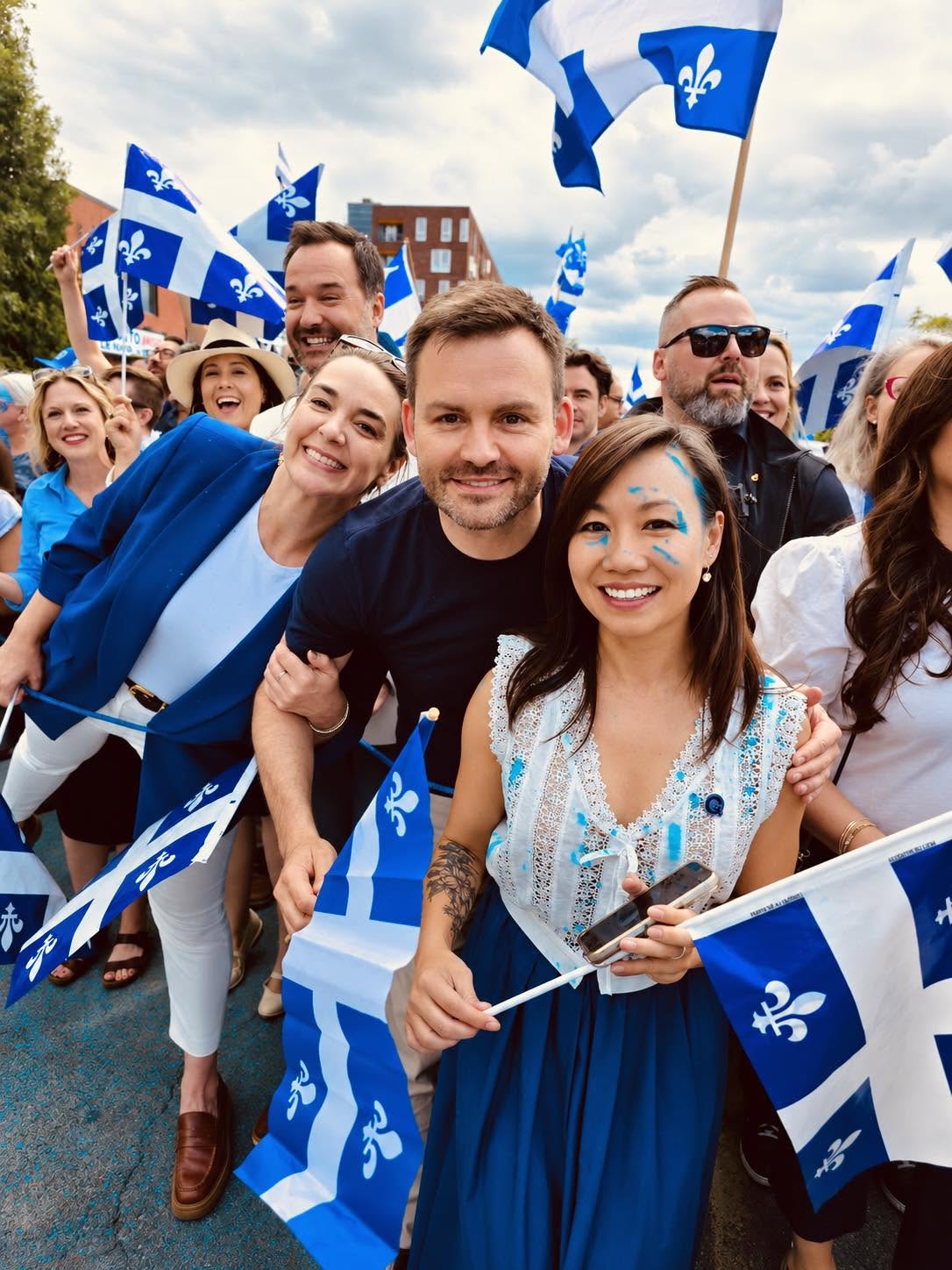 Anne Nguyen entourée de bénévoles lors d'un rassemblement, drapeaux du Québec en main